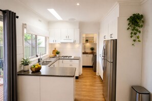 A modern kitchen with white cabinetry, a stainless steel refrigerator, and a wooden floor. - Cosy White Hills Luxury very close to Bendigo (White Hills)