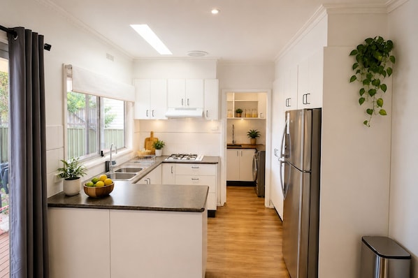 A modern kitchen with white cabinets, a stainless steel refrigerator, a sink, and a window with curtains.