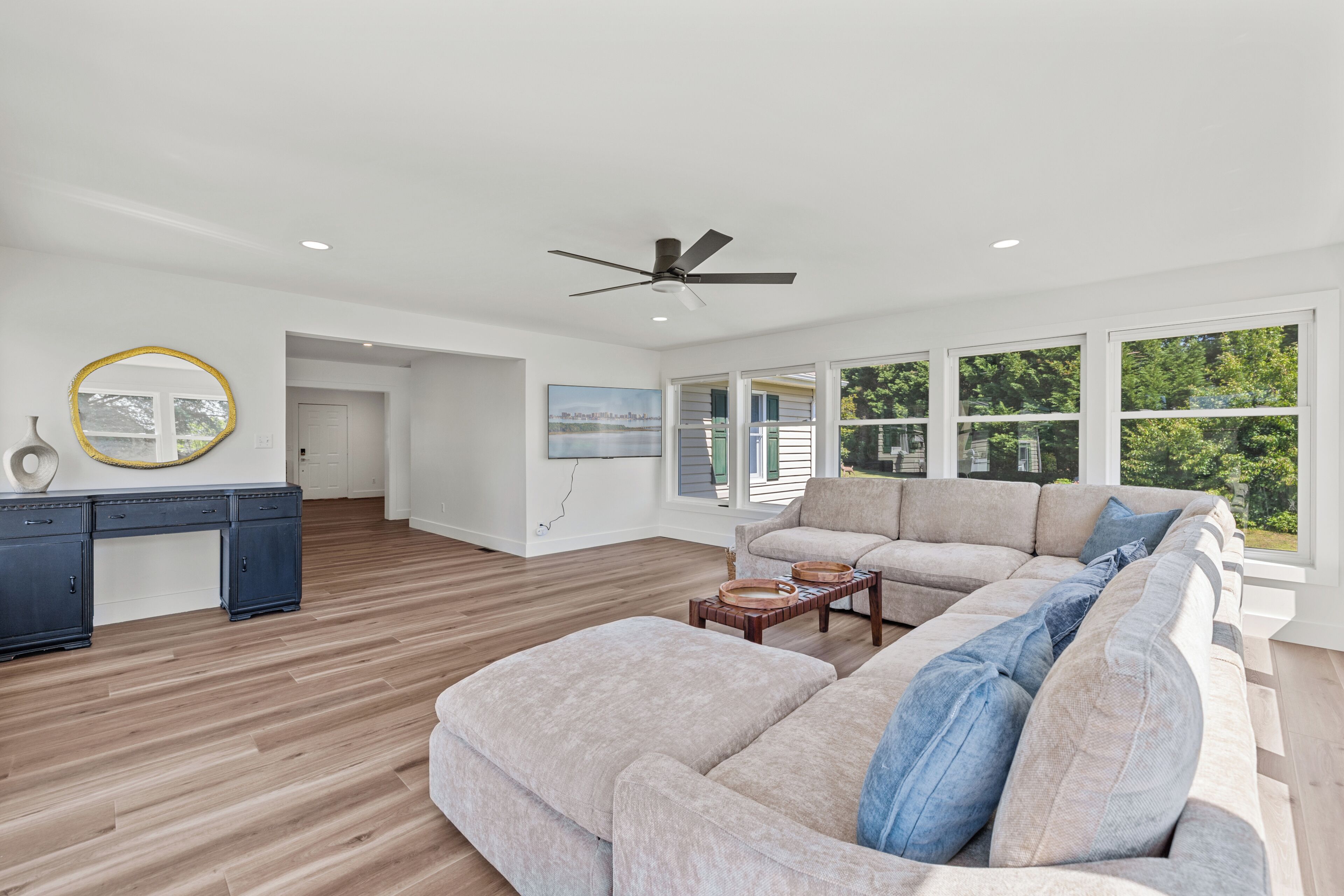 A spacious living room with a large sectional sofa, a desk, and a ceiling fan.