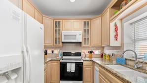 A kitchen with wooden cabinets, a white refrigerator, a microwave, a stove, and a sink. - Dog-Friendly Townhome • Pool & Hot Tub • 5 Minute Walk to Beach (South Padre Island)