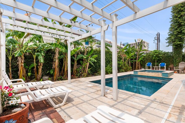 Ein Poolbereich mit weißen Liegestühlen, einer Pergola und Bananenpflanzen.
