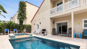 A swimming pool with a tiled deck, surrounded by outdoor furniture and a building with a balcony. - Dog-Friendly Townhome • Pool & Hot Tub • 5 Minute Walk to Beach (South Padre Island)
