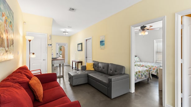 A spacious living area with a grey sectional sofa, a red couch, and a dining area with a small table and chairs. - Dog-Friendly Townhome • Pool & Hot Tub • 5 Minute Walk to Beach (South Padre Island)