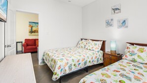 A bedroom with two beds, a ceiling fan, a nightstand with a lamp, a red chair, and a painting on the wall. - Dog-Friendly Townhome • Pool & Hot Tub • 5 Minute Walk to Beach (South Padre Island)