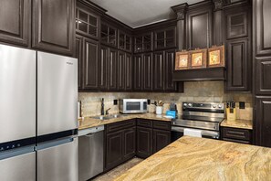A modern kitchen with dark wood cabinets, stainless steel appliances, granite countertops, and a built-in microwave. - Spacious Home w/ Pool, 1/2 Block to Beach (South Padre Island)