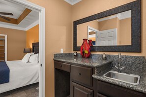 A hotel bathroom with a granite countertop, a sink, a mirror, and a bed with a blue blanket. - Spacious Townhouse • Private Pool • 2 Minute Walk to the Beach (South Padre Island)