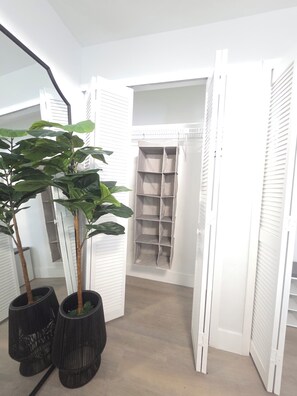 A hallway with a plant, a white closet with open doors, and a shelving unit. - Lovely 3-bedroom house with pool in Cape Coral perfect for your getaway (Cape Coral)