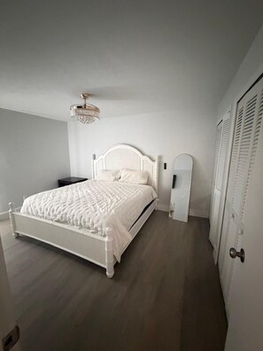 Ein Schlafzimmer mit einem weißen Bett, einer Chandelüster und einer Tür mit Fensterläden.