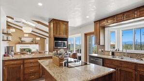 A modern kitchen with wooden cabinets, granite countertops, a built-in microwave, and a large window offering a mountain view. - New! Yosemite Starsong with pool/hot tub/EV/huge views (Coarsegold)