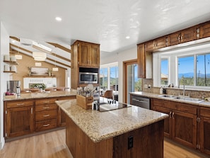A modern kitchen with wooden cabinets, granite countertops, a built-in microwave, and a large window offering a mountain view.