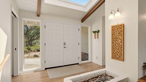 A modern interior with a skylight, white doors, a stone fireplace, and a wooden bench. - New! Yosemite Starsong with pool/hot tub/EV/huge views (Coarsegold)