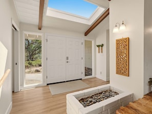 A modern interior with a skylight, white doors, a stone fireplace, and a wooden bench.