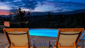 Two wooden lounge chairs with mesh backs facing a swimming pool, surrounded by a deck with a warning sign. - New! Yosemite Starsong with pool/hot tub/EV/huge views (Coarsegold)