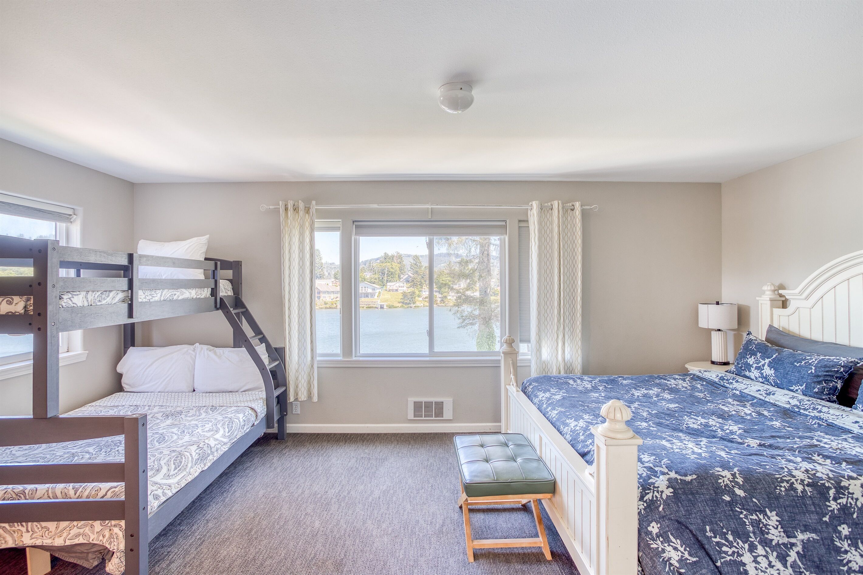 A bedroom with bunk beds, a window with curtains, a bedside lamp, and a view of the outdoors.