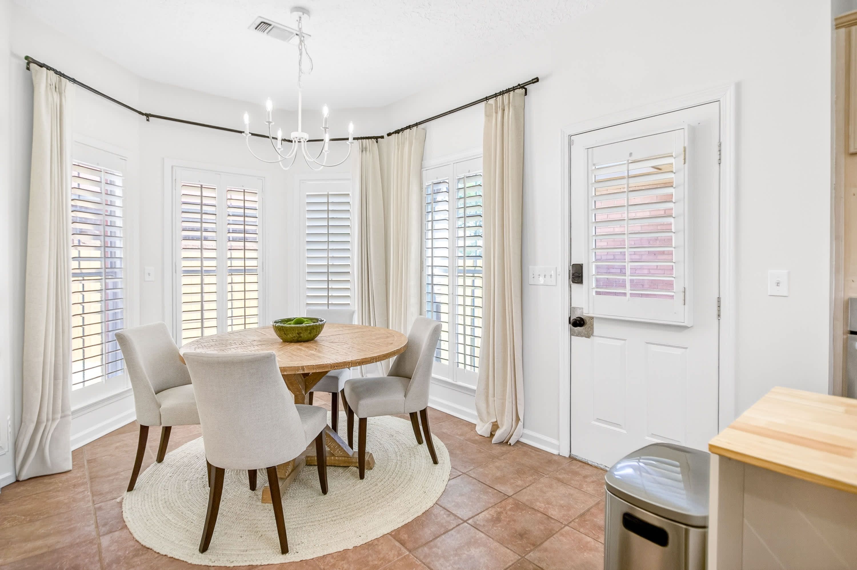 A dining area with a round table, four chairs, a chandelier, and a trash can.