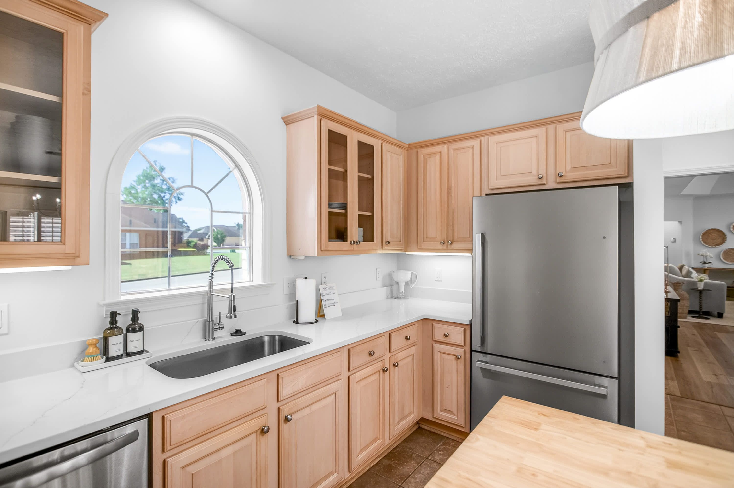 A modern kitchen with wooden cabinets, a stainless steel refrigerator, and a large window.