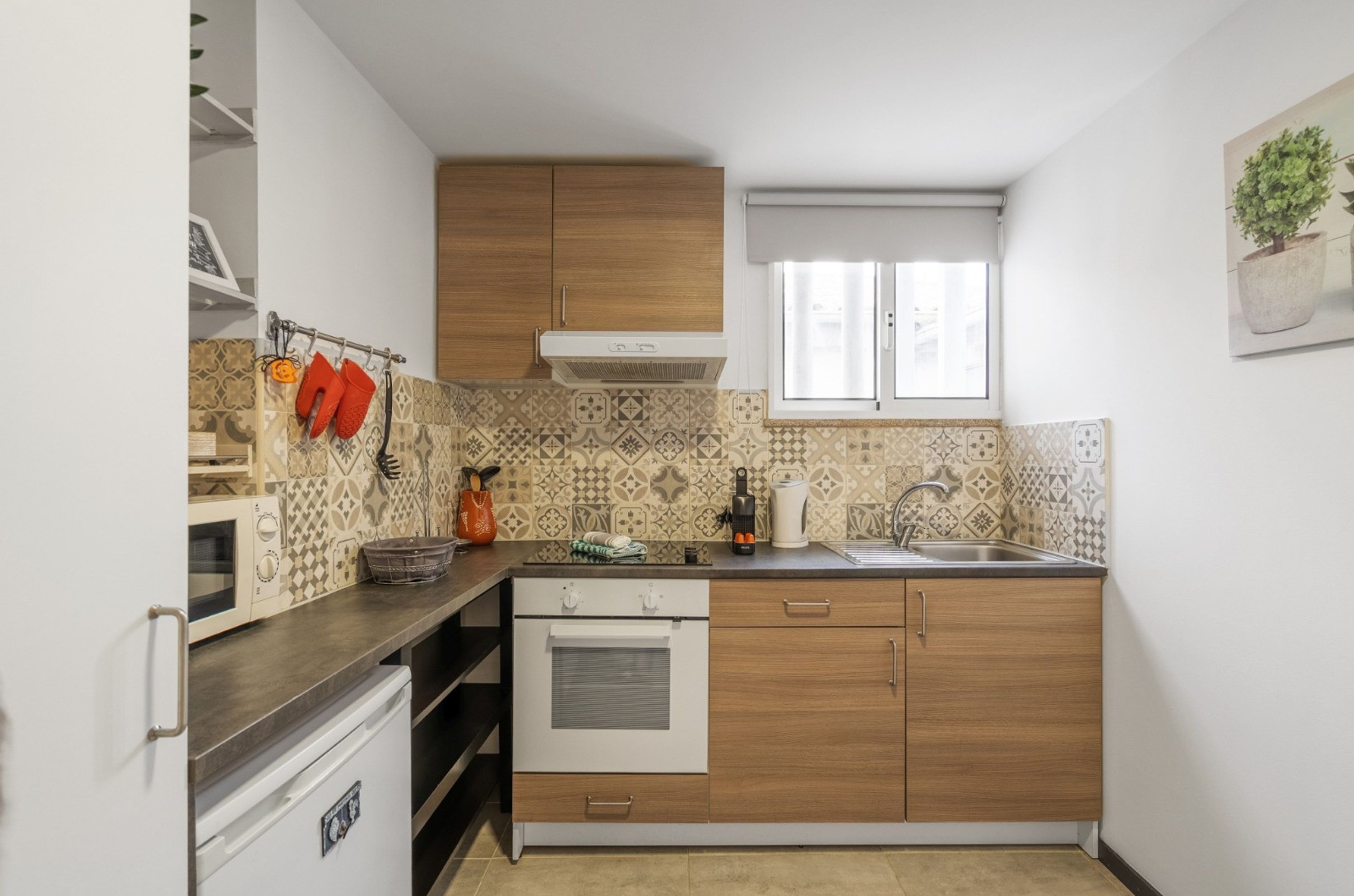 A compact kitchen with a microwave, oven, wooden cabinets, a sink, and patterned backsplash.