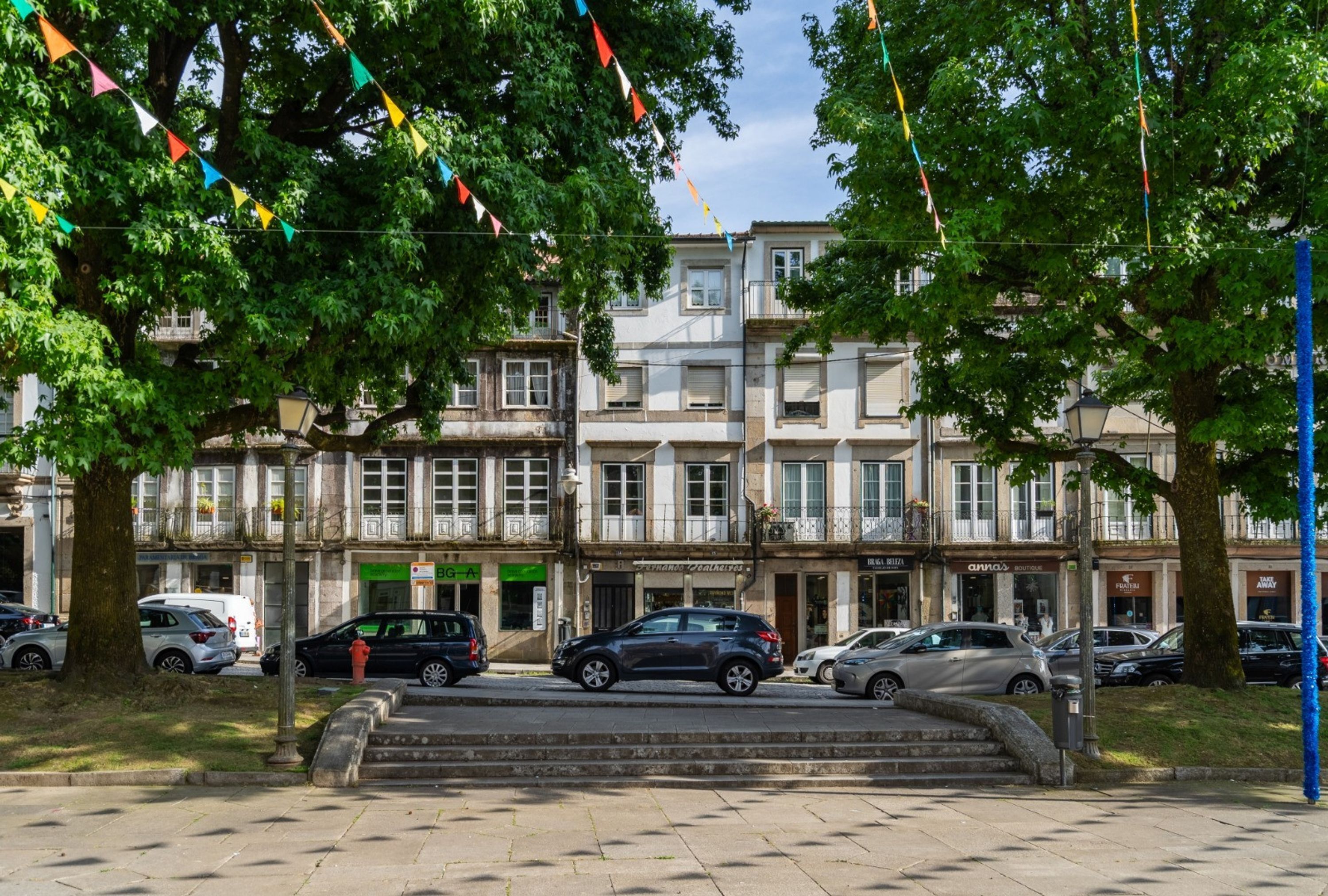 A row of multi-story buildings with parked cars and trees.