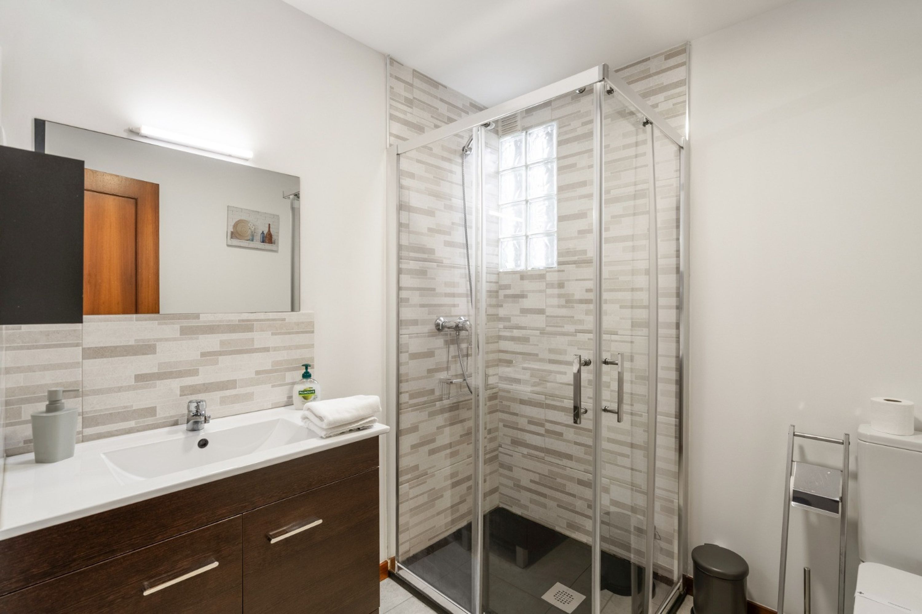 Une salle de bain moderne avec une douche à parois de verre, un lavabo blanc et un meuble-lavabo en bois foncé.