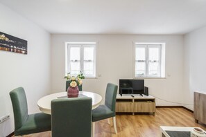 A room with a round table, two green chairs, a TV on a wooden stand, and two windows. - Casa Bracara Augusta by Minho s Guest (Braga)