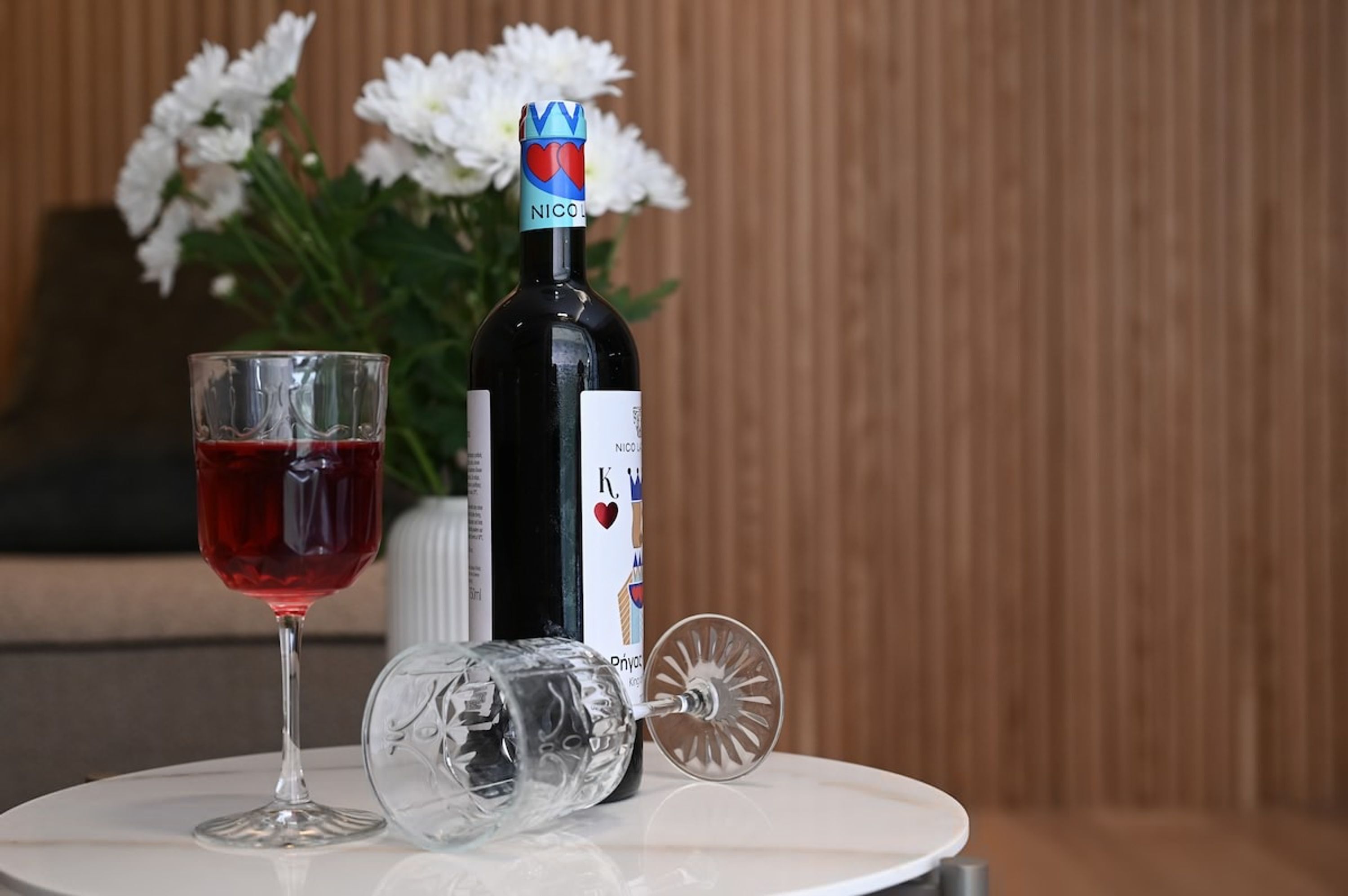 Een fles wijn, een glas rode wijn en een gebroken wijnglas op een tafel met een witte achtergrond en bloemen.
