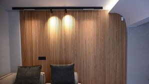 A room with a wooden slat wall, a sofa with two cushions, and a ceiling light fixture. - Cocoon Athenian Riviera by Neuvel (Vari-Voula-Vouliagmeni)