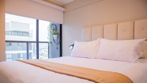 A hotel room with a large bed, a view of the city, and a potted plant on the windowsill. - w Lovely 1BR w Swimming Pool in San Isidro (Lima)