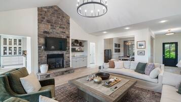 A spacious living room with a stone fireplace, a large sofa, a coffee table, and a television.