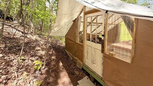 Une petite cabane d’une seule pièce, dotée d’une fenêtre et d’une porte, entourée d’arbres.
