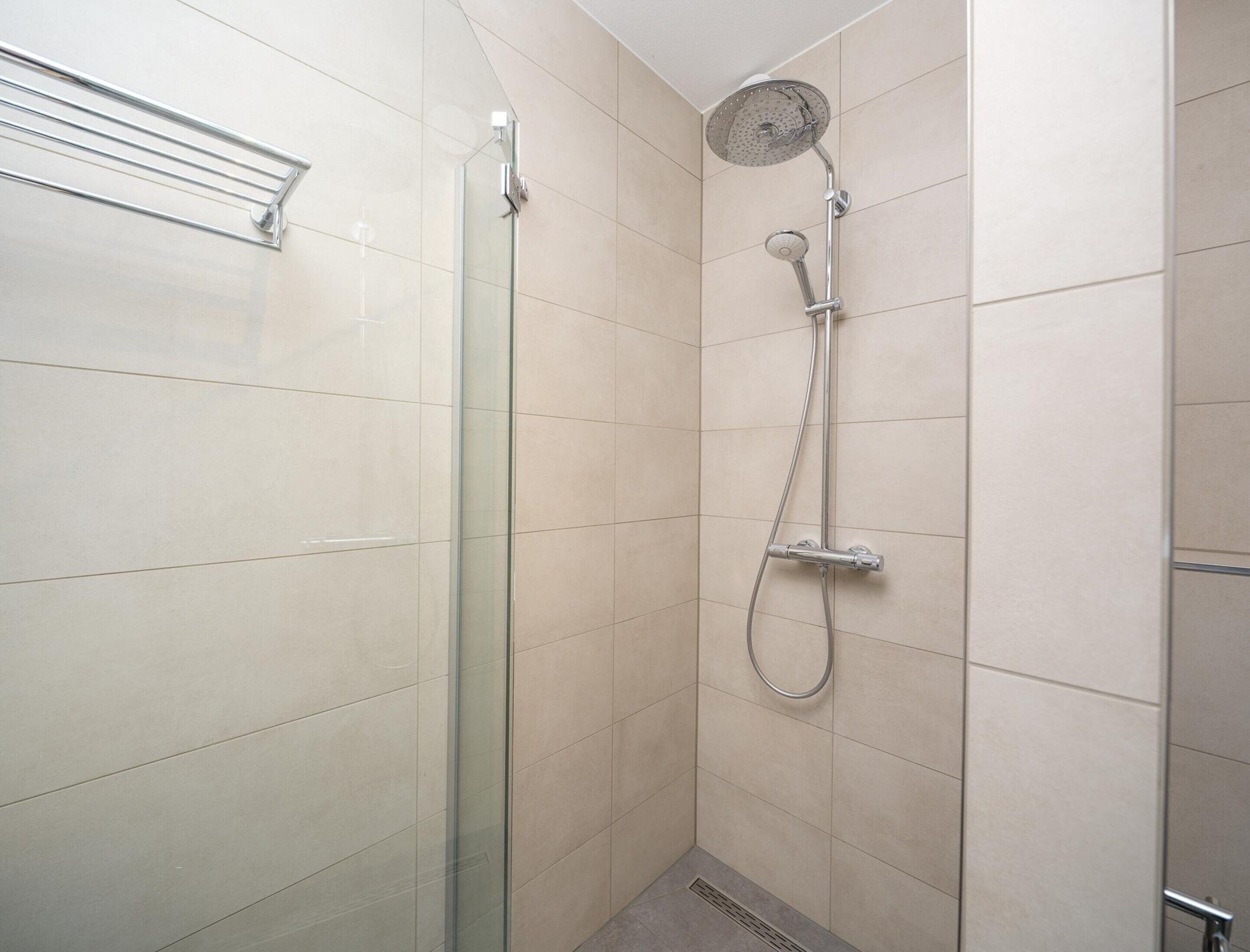 Eine moderne Dusche mit Glastür, Handbrause und wandmontiertem Wasserhahn.