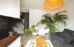 Ein modernes Wohnzimmer mit einem großen Flachbildfernseher, einem grauen Sofa, einem Couchtisch mit einer gewebten Unterlage und mehreren Blumentöpfen.