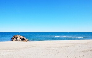 Ein Strand mit einem Felsen und blauem Himmel.