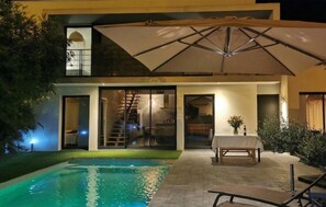 Ein modernes Haus mit Swimmingpool, Sitzgelegenheiten im Freien und einer Treppe, die zu einer oberen Ebene führt.