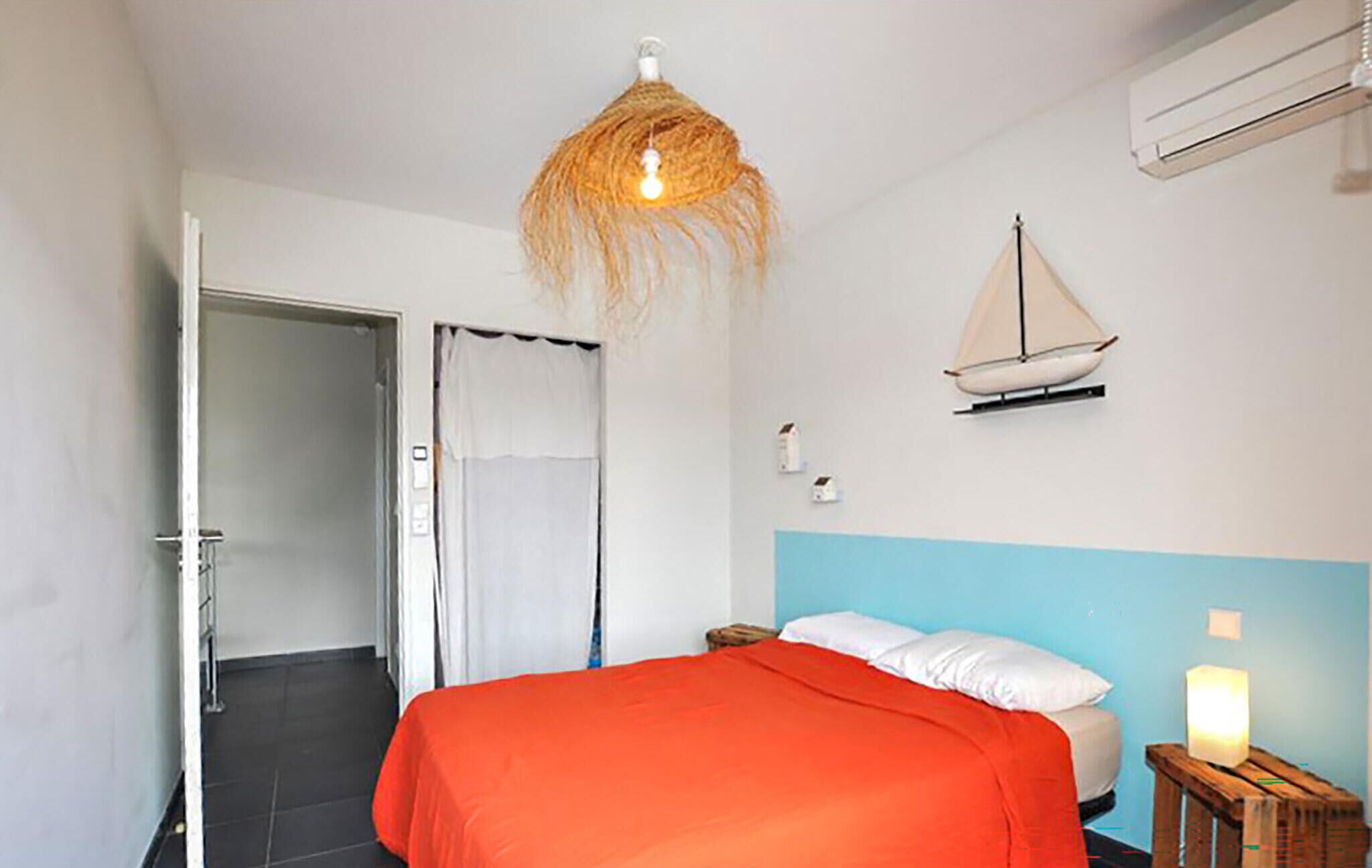 A bedroom with a bed, a hanging light fixture, a sailboat decoration, and a bedside table with a candle.