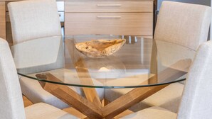 Een moderne eethoek met een tafel met glazen blad, twee gestoffeerde stoelen en een houten bijzettafeltje.