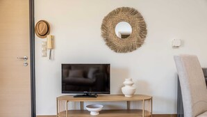 Een kamer met een televisie op een houten standaard, een geweven spiegel, een hoed, een telefoon en een stoel.