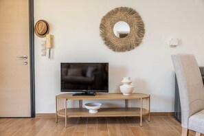 Ein Zimmer mit Fernseher auf einem Holzständer, einem gewebten Spiegel, einem Hut, einem Telefon und einem Stuhl.