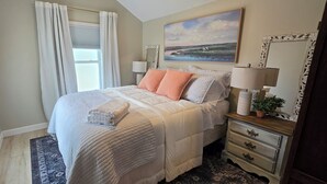 Une chambre à coucher avec un lit, des tables de chevet, un miroir, un tableau et une fenêtre avec des rideaux.