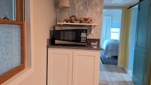 Une cuisine équipée d’un four à micro-ondes, une étagère ornée d’objets décoratifs et une porte donnant sur une chambre.