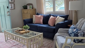 Un salon avec un canapé bleu, un fauteuil blanc, une table basse en verre et un meuble en bois.