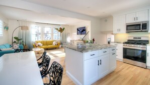 A modern kitchen with white cabinets, a central island, stainless steel appliances, and a dining area with a white table and chairs. - VillaDaWhale Spacious 4bedroom game room house Somers Point bay near Ocean City (Somers Point)