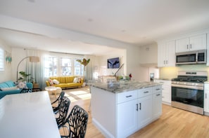 Una cocina moderna con armarios blancos, una isla central, electrodomésticos de acero inoxidable y un comedor con una mesa y sillas blancas.
