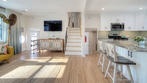 A modern kitchen with white cabinets, a stainless steel microwave, and a bar area with white bar stools. - VillaDaWhale Spacious 4bedroom game room house Somers Point bay near Ocean City (Somers Point)