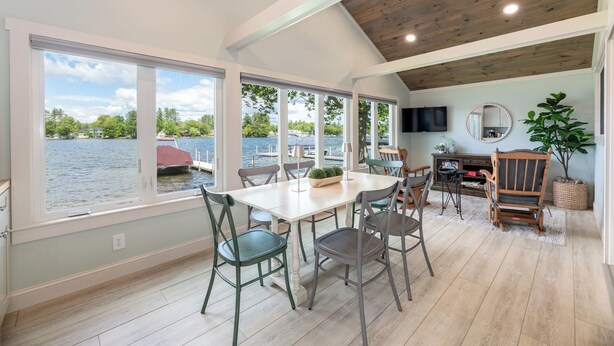 Un coin repas avec vue sur un lac, un plafond en bois et un téléviseur fixé au mur.