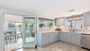 Une cuisine moderne avec des meubles de couleur gris clair, un lave-vaisselle en acier inoxydable et une fenêtre sur laquelle est apposée une enseigne indiquant « WINN SQUAM ».