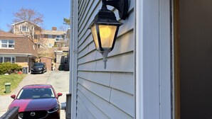A residential exterior with a wooden deck, a red car parked in the driveway, and a black exterior wall-mounted light fixture.