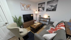 A living room with a sofa, armchair, TV, coffee table, and a world map on the wall.