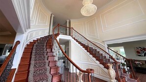 A grand staircase with ornate railings and a chandelier. - Lakefront B&B Room w/Private Island Access + Breakfast Included (Purcellville)