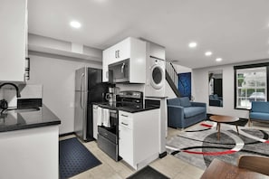 Eine kompakte Küche mit Mikrowelle, Backofen und Waschmaschine, ein blaues Sofa und ein kleiner Couchtisch.