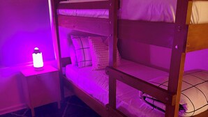 Una cama individual superpuesta con una mesita de noche y una lámpara, en una habitación de tonos morados.